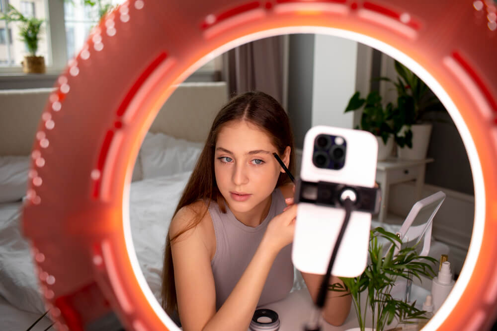 A young female influencer putting on make-up in front of a smartphone and lights