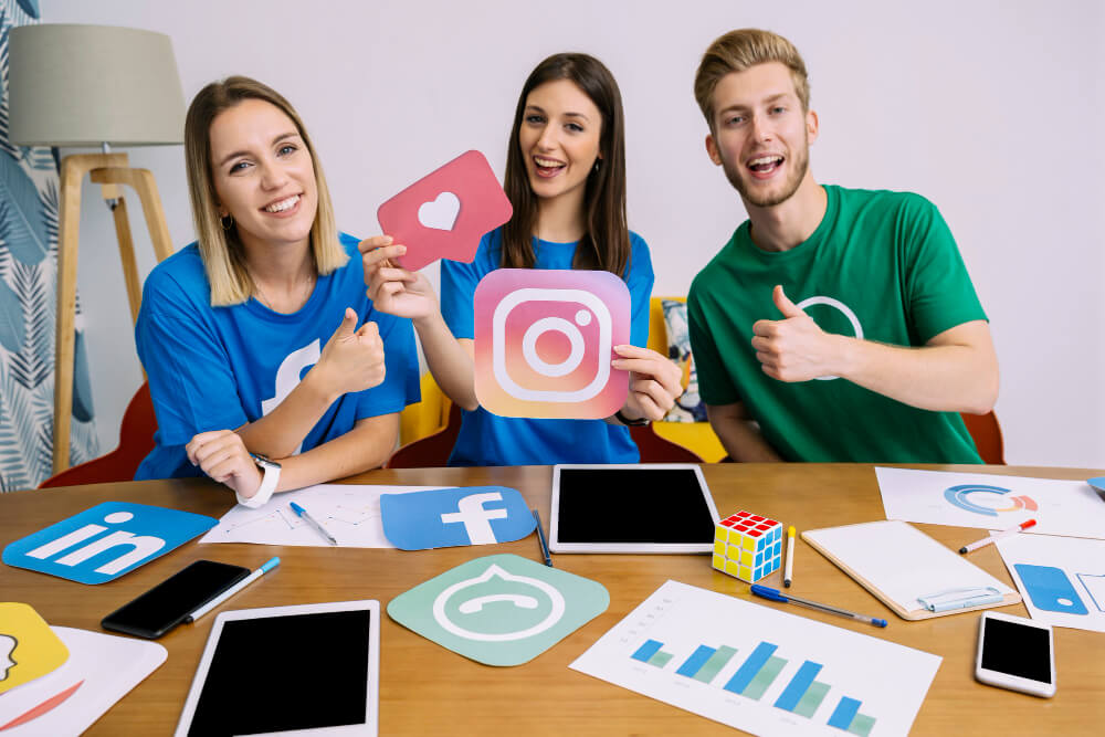 A woman holding up the Instagram icon while her two friends give the thumbs up sign