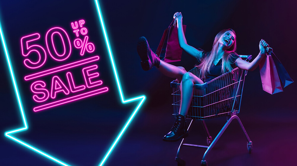 A happy woman holding shopping bags and sitting inside a shopping cart