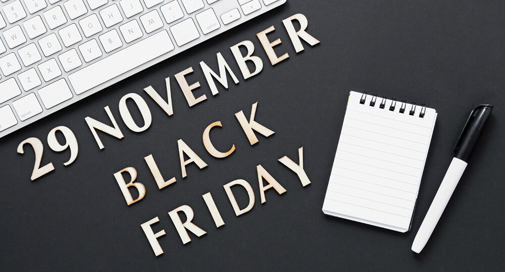 A white keyboard, notepad, white pen, and the words "29 November Black Friday" on top of a black table