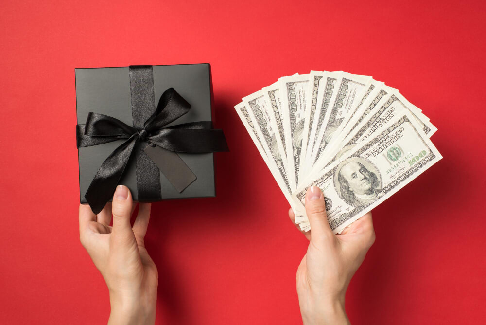 A pair of hands, one holding a black gift box, another holding money