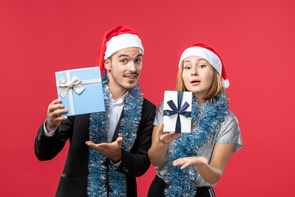 A man and a woman wearing Santa hats holding up Christmas gifts