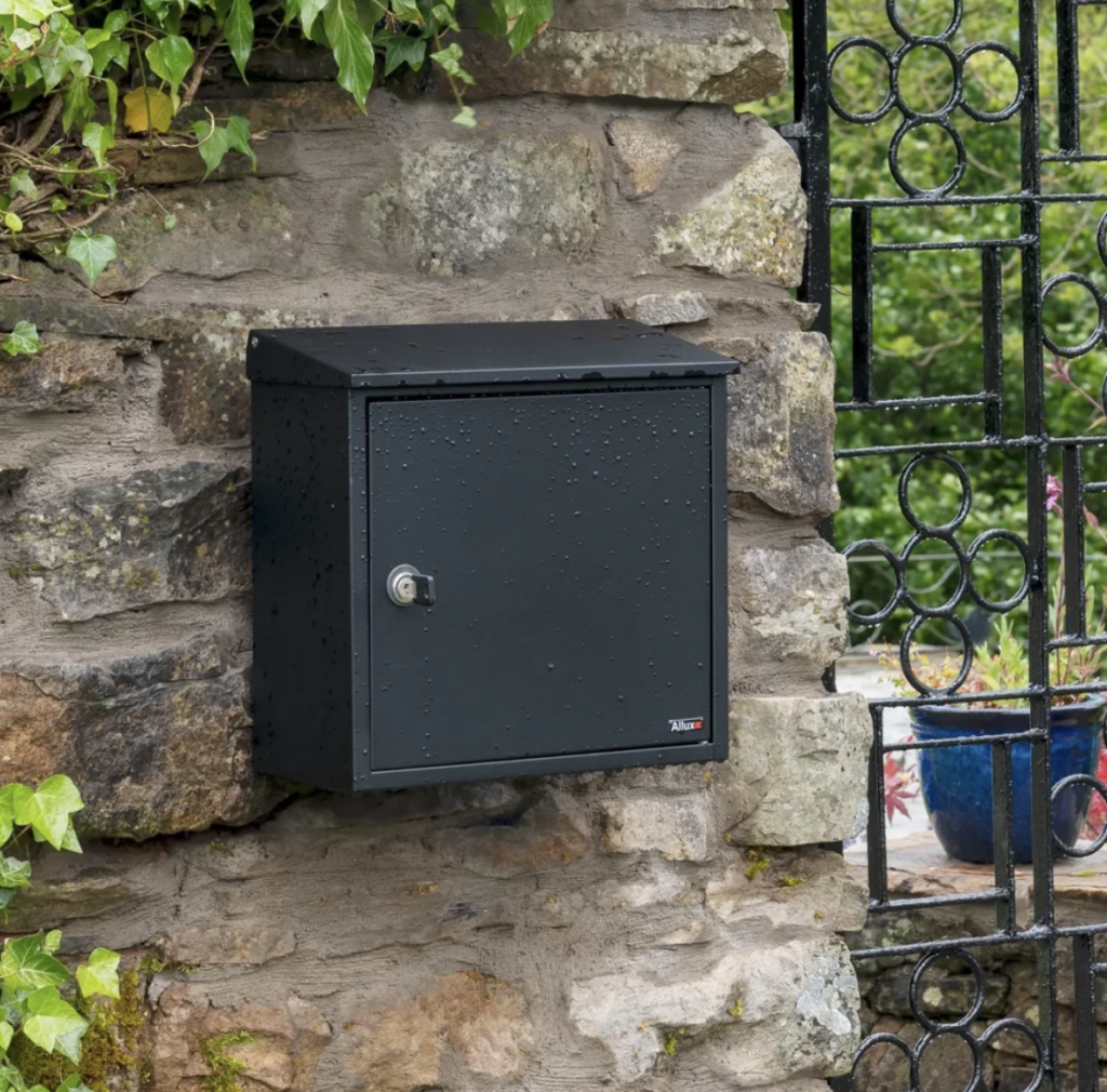 Close-up of a black wall-mounted post box with water droplets, showcasing the product’s waterproof features.
