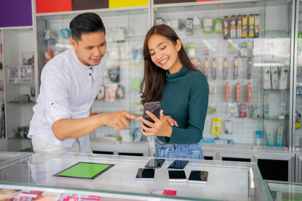 recurring-customers-buying-new-phone - AdTribes A woman smiling and buying a new phone as a man helps her