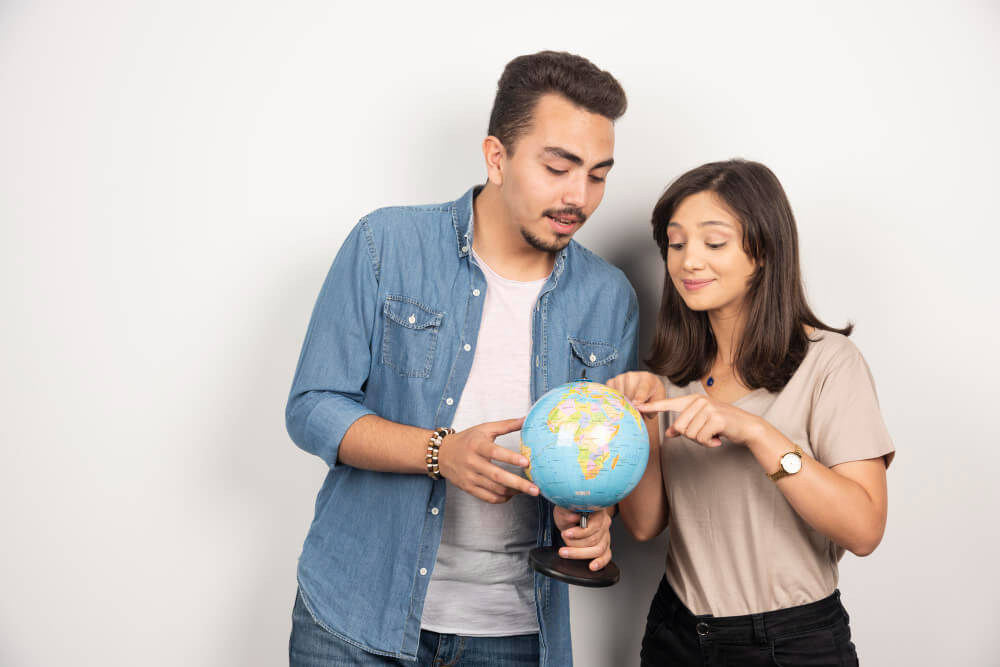 sell-internationally-pick-country - AdTribes A man holding a globe while a woman points at a spot on the globe