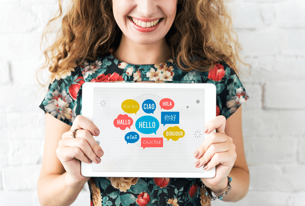 A woman holding up a tablet showing the word "hello" in various languages